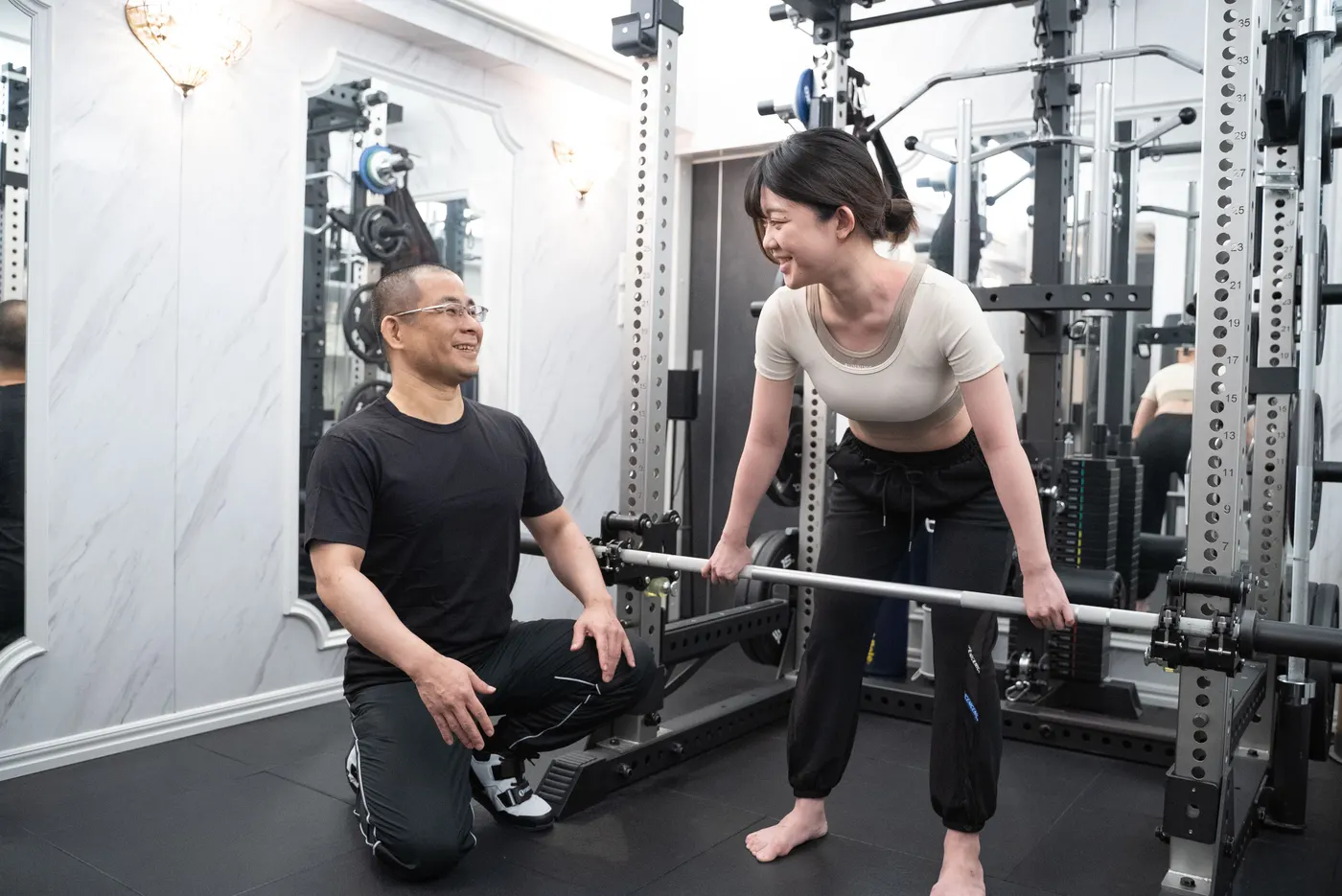 PriGym（プリジム）のセッション風景。笑顔で指導を受けながらバーベルを持ち上げるトレーニング。